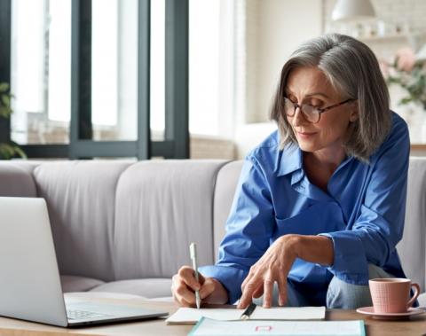 A woman using a laptop and writing notes. 